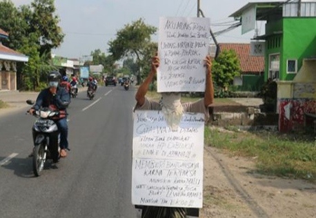 Zainuri saat berjalan kaki menuju Kantor Desa Bandung Kencur sambil membawa poster.